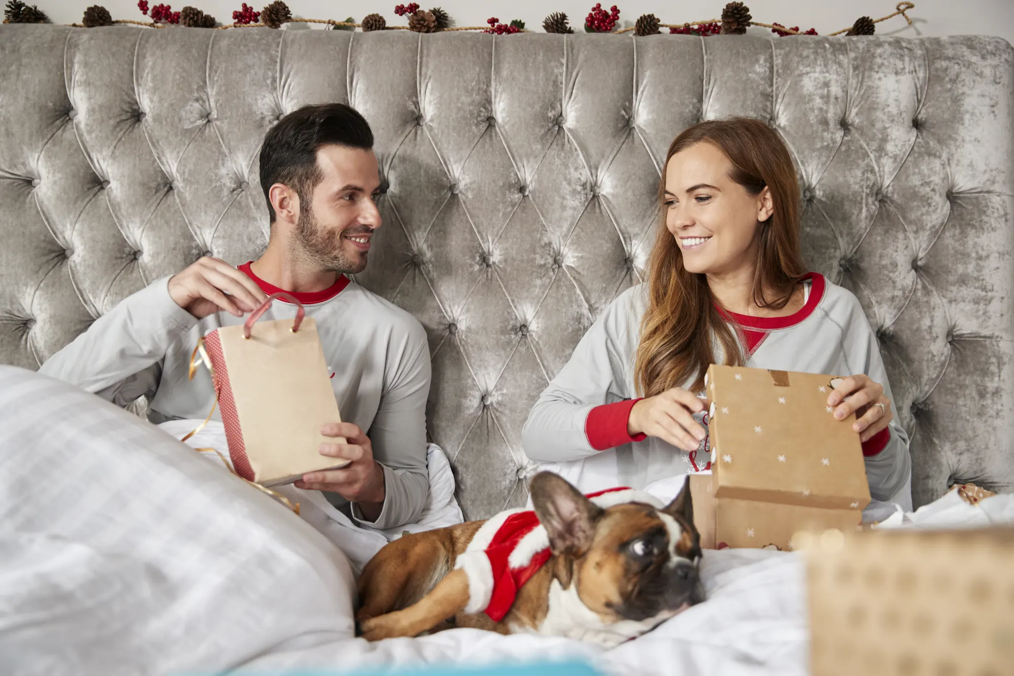 Dog dad and mom in bed opening gifts with their puppy on their lap